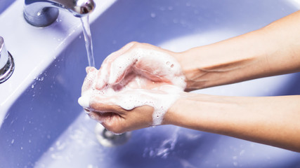 Primer plano levemente elevado de un par de manos de mujer lavandose con jabón sobre una bacha celeste