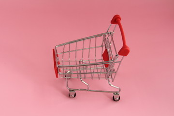 Small trolley with a shopping basket for buy in store on a pink background