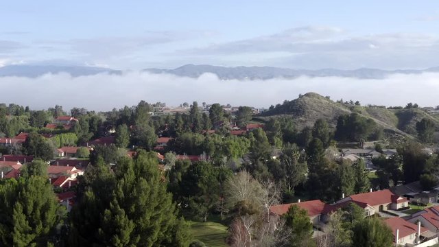 Los Angeles city neighborhood in mountains with morning misty clouds, aerial view
