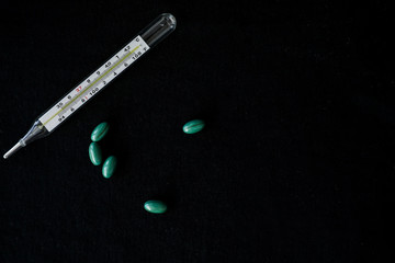 A thermometer and bright green pills, isolated on a black background