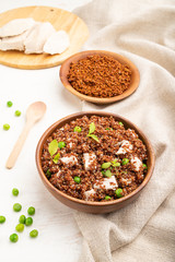 Quinoa porridge with green pea and chicken in wooden bowl on a white wooden background. Side view.