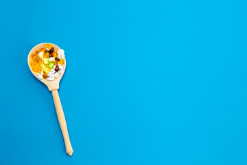 In a wooden spoon on a blue background are medical medicines of different colors. Healthcare concept. Copy space.