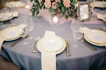 Elegant wedding table decorated with blue tablecloth, white plates and silver cutlery, candles and pink roses