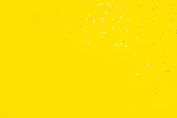 Tiny pearl stars on yellow background. Flat lay, top view.