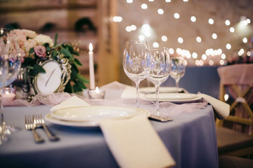 Beautifully decorated wedding table with glasses, candles, flowers, tableware and a plate with napkin