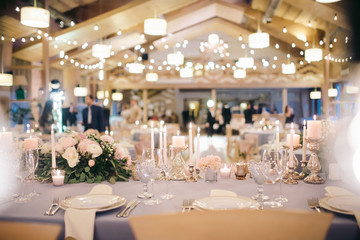 flower arrangement stands on the table in wedding banquet area in a restaurant, the table is decorated with candles, there are plates, glasses, cutlery, lights