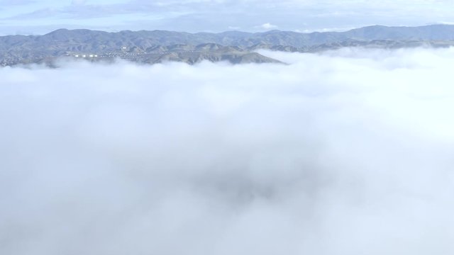 Aerial cloud descent, mountains covered in morning mist, revealing neighborhood of houses, Los Angeles