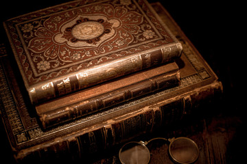A vintage pile of three old brown leather books with eye glasses on a wood table.