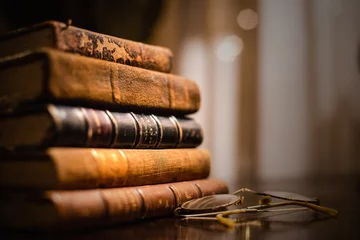 Foto op Canvas Een vintage stapel van vijf oude bruinleren boeken met een bril op een houten tafel. © Sacher
