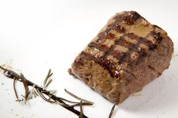 Grilled beef steak with rosemary. Grilled striploin sliced steak. Juicy thick grilled T-bone beef steak seasoned with rosemary fresh of the summer BBQ. Vegetables on a black plate with salt and pepper