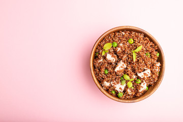 Quinoa porridge with green pea and chicken in wooden bowl on a pink background. Top view, copy space.