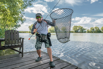 Fisherman with pike fish in fishing landing net.