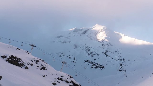 Timelapse of the clouds moving trough the valley with the sun breaking trough, ski lift starts running in front