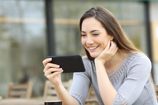 Happy woman watching video on phone in a coffee shop