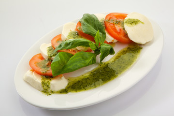 Caprese Salad with Tomatoes, Mozzarella Cheese, Rocket Salad, basil leaves, dressed with Pesto Sauce on rustic wooden background.  Traditional Italian cuisine. Flatlay healthy vegetarian dish.