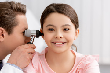 ent physician examining ear of cheerful kid with otoscope
