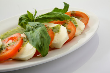 Caprese Salad with Tomatoes, Mozzarella Cheese, Rocket Salad, basil leaves, dressed with Pesto Sauce on rustic wooden background.  Traditional Italian cuisine. Flatlay healthy vegetarian dish.