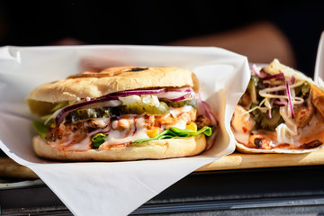 Close up of a tasty hamburger or burger sandwich, with grilled spiced meat with mayonnaise, pickled cucumbers, red onion and green salad, displayed for sale at a street food market, selective focus