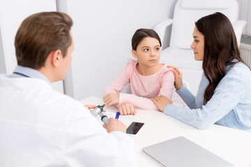 Fototapeta premium smiling mother touching daughters shoulder during consultation with ent physician