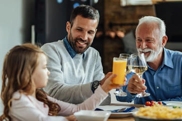 Happy man toasting with his small daughter and senior father during lunch.