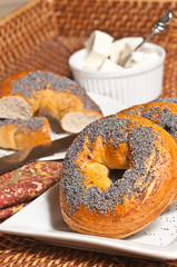 Top view, close up of a freshly baked bagel, with seeds on a round, white plate with a cup of cream cheese, on a print, cloth napkin