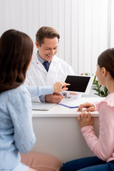 back view of mother and daughter near ent physician showing digital tablet with blank screen