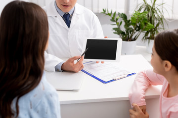 Obraz premium selective focus of woman with daughter near smiling otolaryngologist showing digital tablet with blank screen