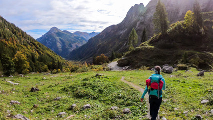 A woman in hiking outfit wandering in Italian Alps. Sharp slopes on both sides of the valley. Hard to reach mountain peaks. There are many mountain ranges in the back. Serenity and calmness. Freshness