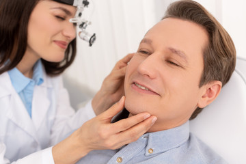 Fototapeta premium selective focus of attractive otolaryngologist in ent headlight examining ear of smiling man