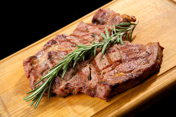Grilled beef steak with rosemary. Grilled striploin sliced steak. Juicy thick grilled T-bone beef steak seasoned with rosemary fresh of the summer BBQ. Vegetables on a black plate with salt and pepper