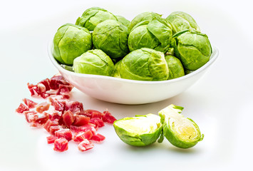 Bowl with raw brussels sprouts, fresh, whole and cut in two halves (cabbages - Brassica oleracea) and ham tacos. Isolated on white background.