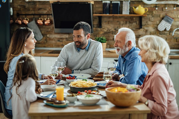 Happy multi-generation family enjoying in conversation during lunch at dining table.