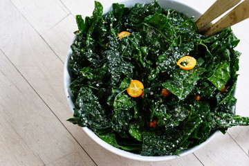 Fresh green kale salad with sliced kumquat fruit in a bowl