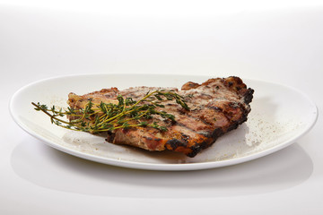 Grilled beef steak with rosemary. Grilled striploin sliced steak. Juicy thick grilled T-bone beef steak seasoned with rosemary fresh of the summer BBQ. Vegetables on a black plate with salt and pepper