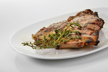 Grilled beef steak with rosemary. Grilled striploin sliced steak. Juicy thick grilled T-bone beef steak seasoned with rosemary fresh of the summer BBQ. Vegetables on a black plate with salt and pepper