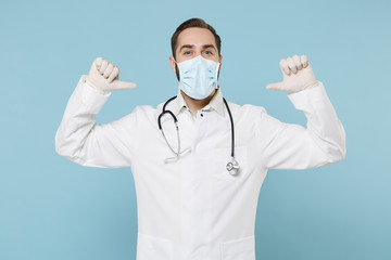 Male doctor man in white medical gown sterile face mask gloves isolated on blue background. Epidemic pandemic spreading coronavirus 2019-ncov sars covid-19 flu virus concept. Point thumbs on himself.