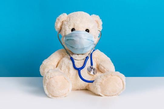 Cute teddy bear doctor with protective medical mask and stethoscope. Concept of pediatric treatment, hygiene and virus protection for child patient during epidemic. Fluffy toy on blue background