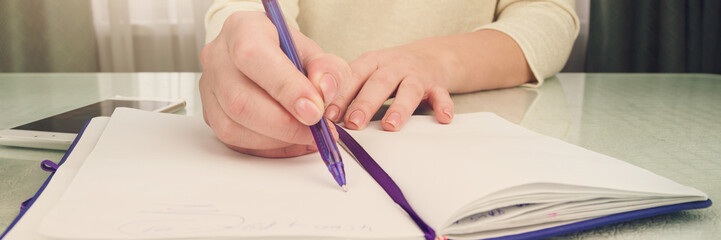 lady writes in notepad with purple pen sitting at table with smartphone and lavender