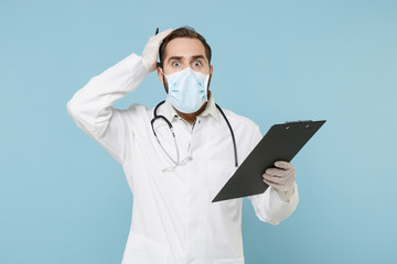 Shocked doctor man in gown face mask gloves isolated on blue background. Epidemic pandemic...