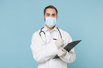 Male doctor man in medical gown face mask gloves isolated on blue background. Epidemic pandemic coronavirus 2019-ncov sars covid-19 flu virus concept. Hold clipboard with medical document health card.