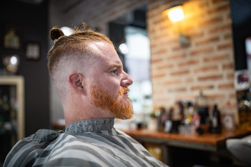 side view of redhead man sitting in modern barbershop waiting for barber