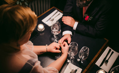 couple on a date, sit on a table holding hands, man wears suit, girl wears dress