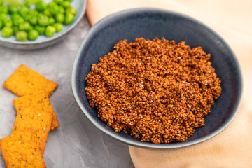 Raw quinoa in ceramic bowl on a gray concrete background and orange textile. Side view.