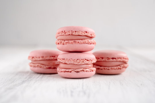 Pink tasty macaroons stacked in pile against wooden white surface