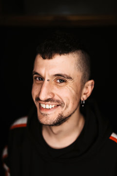 Confident adult male with piercing and mohawk smiling and looking at camera in dark room