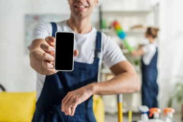 cropped view of happy cleaner holding smartphone with blank screen