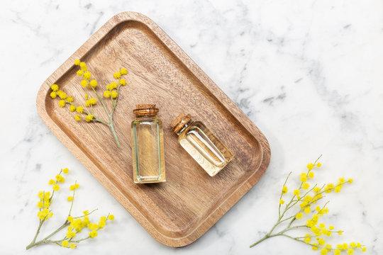From above top view of mimosa flower and its essential oil on wooden tray on marble background table