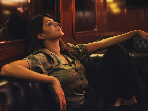 Side view of tired relaxed woman leaning on back of leather black sofa and looking away in cafe