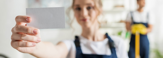 panoramic shot of attractive cleaner in uniform holding blank card