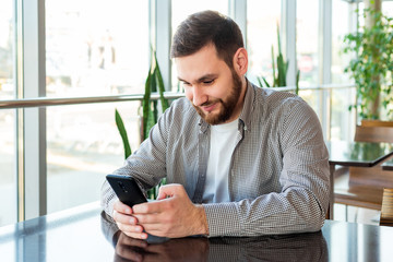 Smart phone texting. Attractive bearded caucasian businessman using smartphone while sitting in office. Businessman using mobile phone app in urban city cafe.Man texting message using smart phone